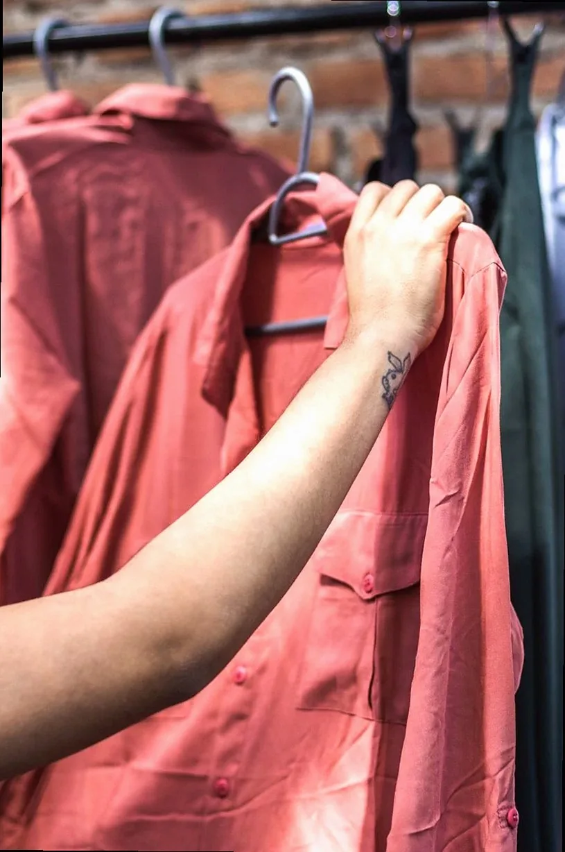 A close-up shot of a hand holding a salmon-colored shirt on a clothing rack.
